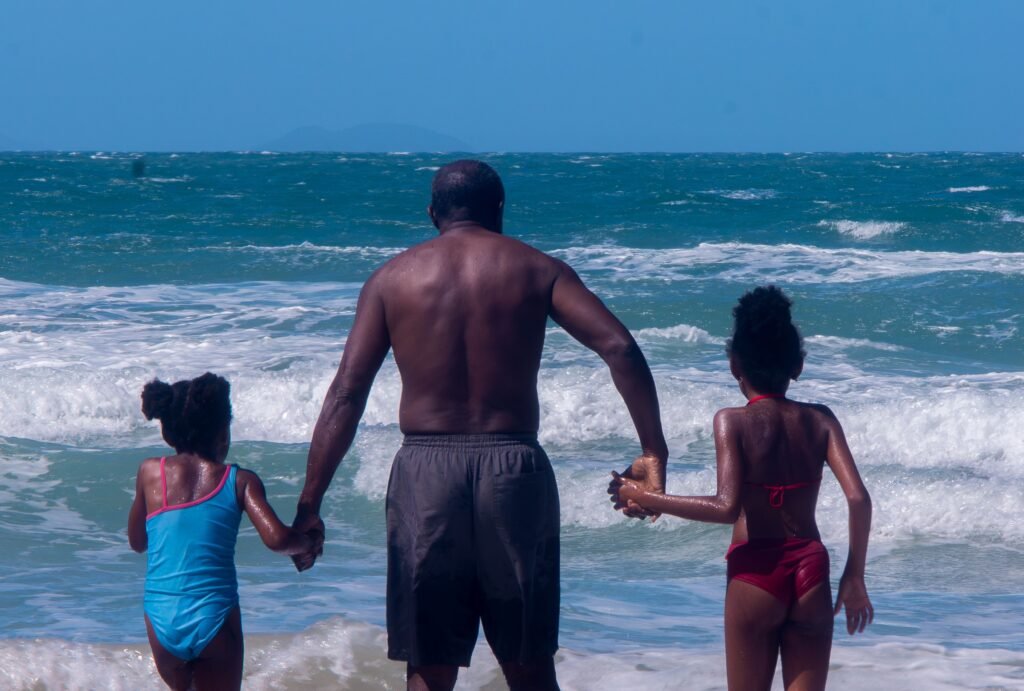 A father and two children holding hands at the beach, enjoying a summer day.