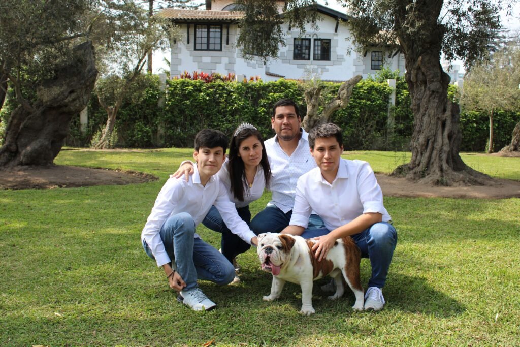 A family posing with a bulldog in a sunny garden setting.